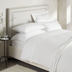 a bed with white sheets and pillows on top of it next to a night stand