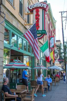 people sitting at tables in front of a restaurant with an american flag hanging from the ceiling