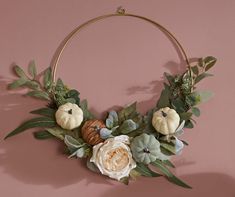 a wreath with flowers, leaves and acorns hangs on a wall in front of a pink background