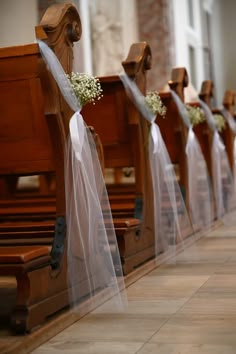 a row of wooden pews with white flowers on them and veils over the seats