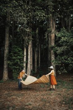 two people standing in the woods with a large kite hanging from it's side