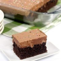 a piece of chocolate cake sitting on top of a white plate next to a glass dish