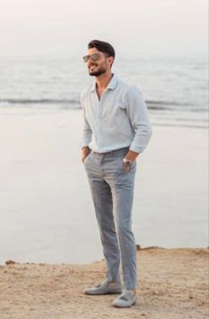 a man standing on the beach with his hands in his pockets and looking off into the distance