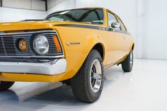 an old yellow muscle car is parked in a white room with no one around it