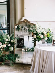 a mirror sitting on top of a table next to flowers and greenery in front of it