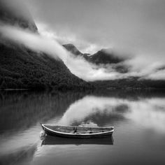 a small boat floating on top of a body of water under a cloudy sky with mountains in the background