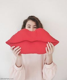 a woman holding up a red pillow to her face with the shape of a kiss on it