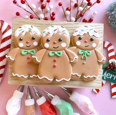 three decorated gingerbread men on a wooden board with candy canes in the background