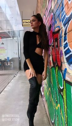 a woman leaning against a wall with her legs crossed and wearing thigh high black boots