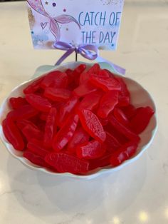 a bowl filled with red gummy bears sitting on top of a table next to a sign that says catch of the day