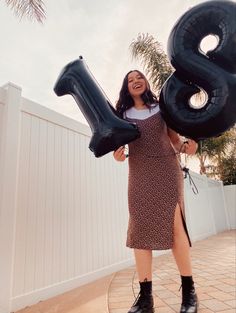 a woman holding two large black balloons in the shape of an 8, and standing next to a white fence