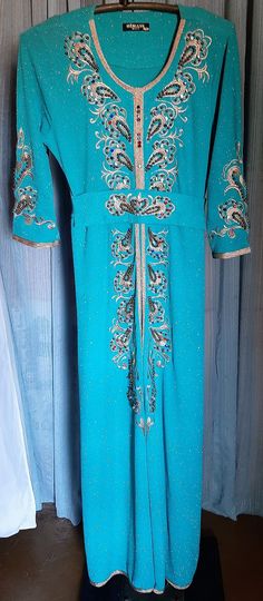 This is just a gorgeous dress and belt.  The color is gorgeous turquoise with metallic glitter woven in.  The dress is jeweled with beads and gems and all appear intact.  The only real issue I found was on the hemline  (see pic)  looks like a heel got caught.  Armpit to armpit is 19 inches.  Waist is 34 inches.  It has a tie on belt.  Has a front opening.  It's trimmed in gold cord and embroidered and adorned with beads and gems and rhinestones. Hips are 40 inches.  Sale is final. Turquoise And Gold Dress, Dress And Belt, Embroidery Beads, Turquoise And Gold, Turquoise Dress, Gold Dress, Dress Clothes For Women, Gold Trim, Gorgeous Dresses