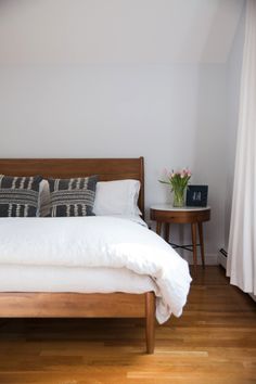 a bed with white linens and pillows in a bedroom next to a wooden table