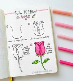 an open notebook with some markers and pens on it next to a drawing book that says how to draw a rose