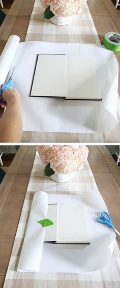 someone cutting out an open book on top of a table with flowers in the background