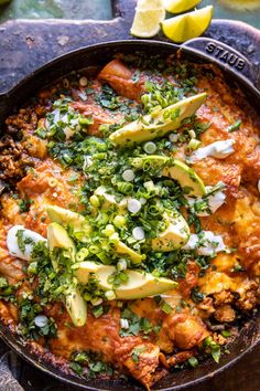 a skillet filled with meat and vegetables on top of a wooden table next to lemon wedges