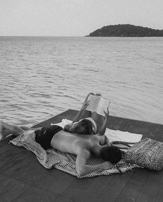 black and white photograph of two people laying on a dock reading a book while looking out at the water