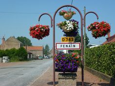 a street sign sitting on the side of a road with flowers hanging from it's sides