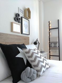 a white bed topped with lots of pillows next to a night stand and pictures on the wall