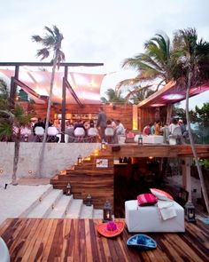 a group of people sitting at tables on top of a wooden deck next to palm trees