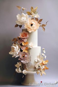 a three tiered white cake with flowers on the top and bottom, in front of a gray background