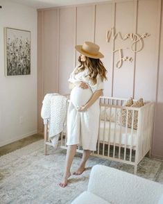 a woman standing in front of a crib with her belly wrapped up and wearing a hat