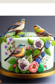 two birds are sitting on top of a decorated cake with flowers and leaves around it