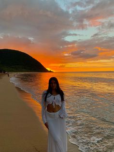 a woman standing on top of a sandy beach next to the ocean at sun set