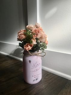 a pink mason jar filled with flowers sitting on top of a wooden floor next to a white wall