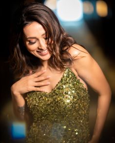 a woman in a gold dress smiling and holding her hand on her chest while looking at the camera