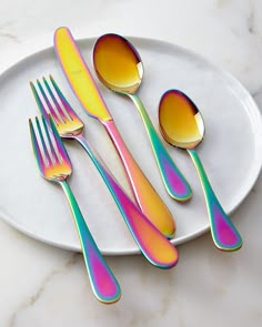 three forks and two spoons on a white plate with multicolored paint over them