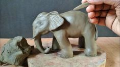 a person holding a pair of scissors over an elephant figurine on a table