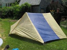 a yellow and blue tent sitting on top of a lush green field next to a house