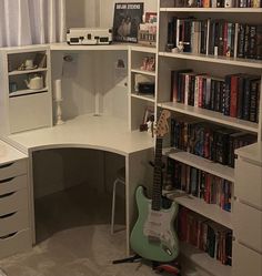 a guitar sits in the corner of a room with bookshelves and desks