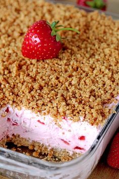 a dessert with strawberries and crumbs in it on a wooden table next to other fruit