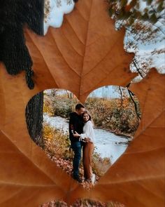 a couple standing next to each other in front of a heart shaped leaf