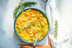 a bowl of soup with carrots and other vegetables on a white cloth next to a knife