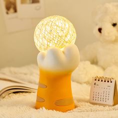 a yellow lamp sitting on top of a bed next to a calendar and teddy bear