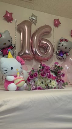 hello kitty balloons and flowers on a table in front of a large number 16 sign