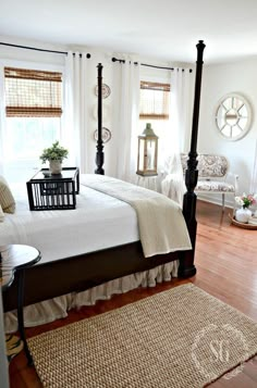 a bedroom with four post bed, white walls and wood flooring is pictured in this image