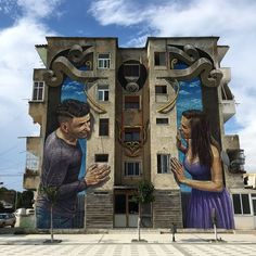 two people standing in front of a building with large murals on it's side