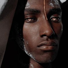 a man with white powder on his face wearing a yellow head piece and gold earring