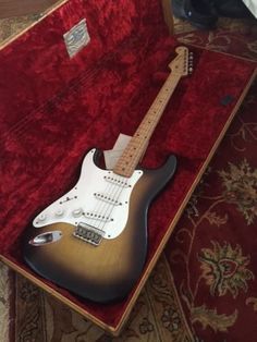 an electric guitar sitting in a case on top of a red carpeted floor next to a rug