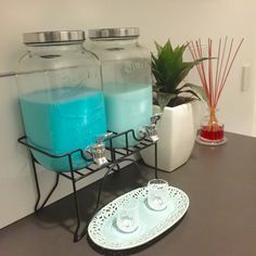 two jars with blue liquid are sitting on a counter next to a plate and vase