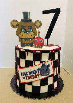 a birthday cake with a teddy bear and number seven on the top is decorated in black and white checkerboard