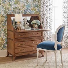 a blue chair sitting in front of a wooden dresser next to a window with curtains