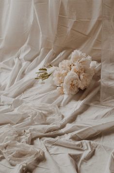 a bouquet of white flowers sitting on top of a bed covered in sheeted sheets