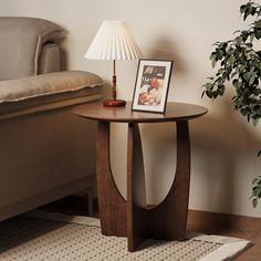 a small table with a lamp on it next to a couch and a plant in the corner