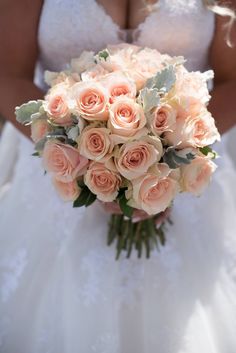 a bride holding a bouquet of peach colored roses