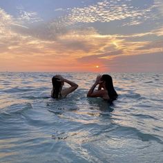 two women in the water at sunset with their backs to each other and one holding her head